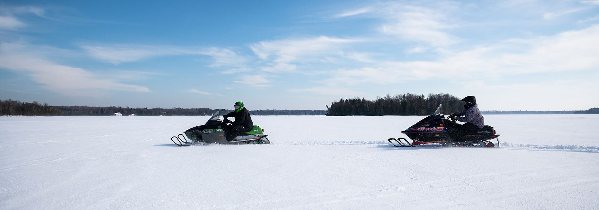 Two snowmobiles driving through the snow.