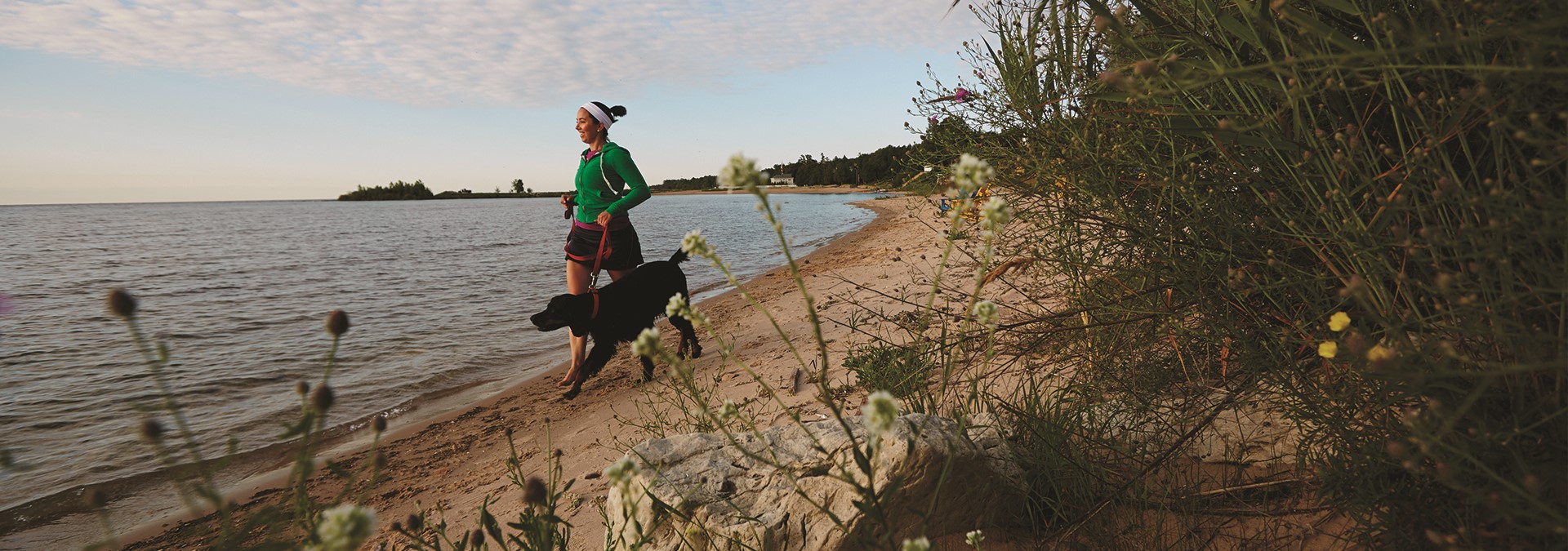 A woman running with a dog on the beach.