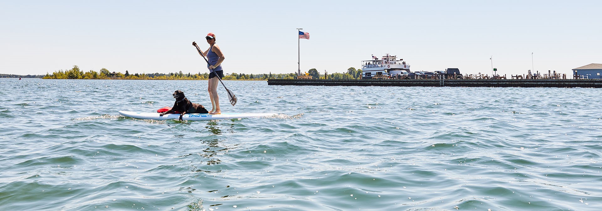 A person on a standup paddleboard with a dog lying on the board.