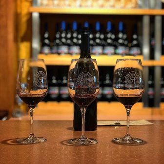 Wine glasses lined up in front of a bottle of wine on a bar.