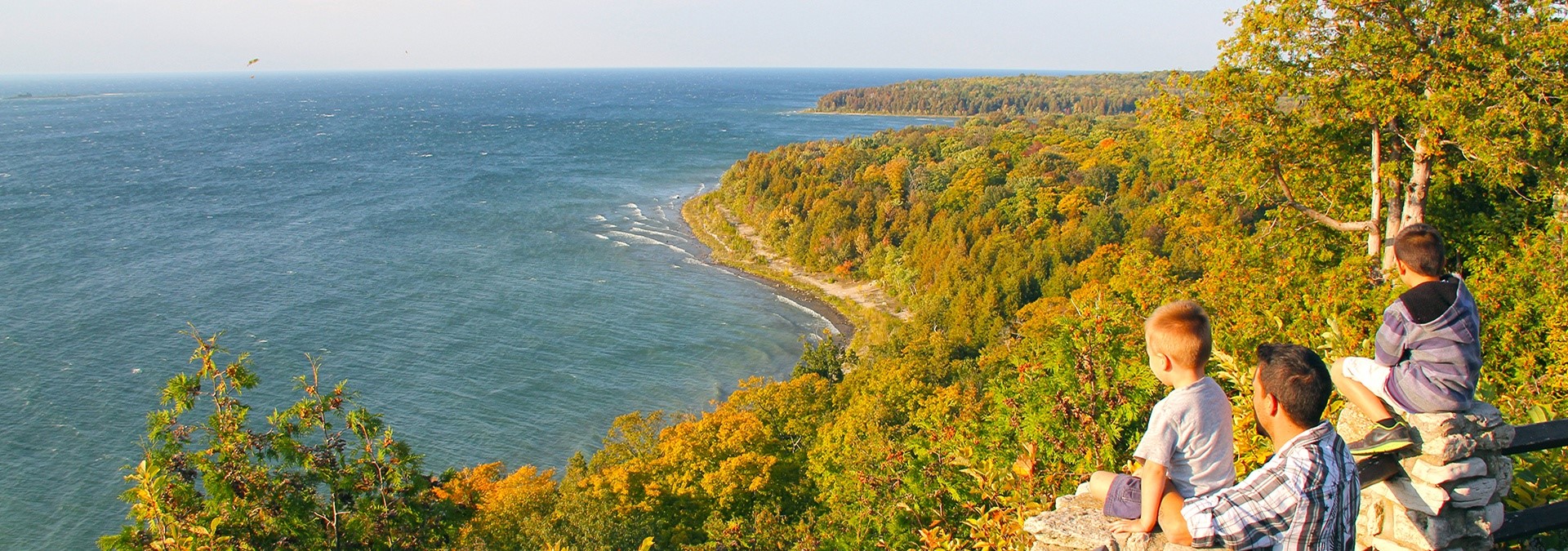 A group of boys sitting on a cliff looking out at the lake