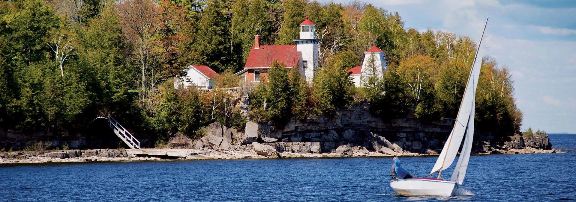 A lighthouse in the distance with a sailboat in the foreground.