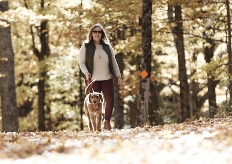 A woman walking her dog on a wooded trail.