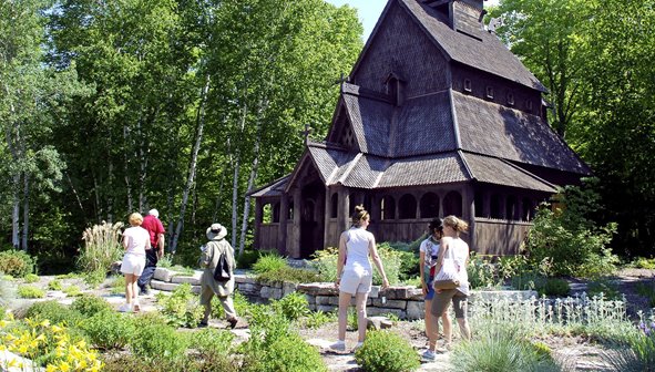 People walking in front of a wooden building surrounded by trees.