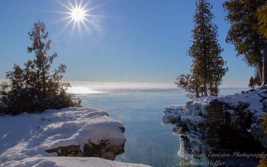 Sun shining over a snowy cliff with trees