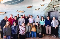 A group of people standing in front of a wall painted with fish.