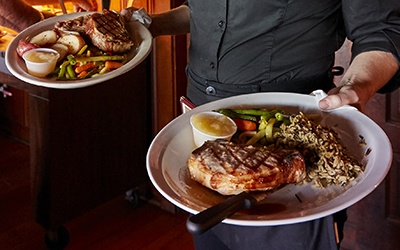 A server presents two pork chop entrees at a supper club.